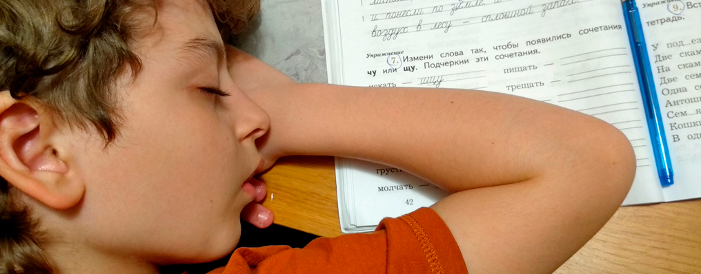 Menino deitado e dormindo exausto sobre o caderno de exercícios na mesa