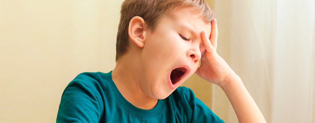 enino bocejando com a boca aberta e a mão na testa, demonstrando tédio em aula